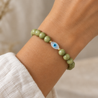 The Romy Bracelet worn on a wrist. This is a green bracelet with a pearl evil eye accent and tiny gold beads surrounding the accent. 