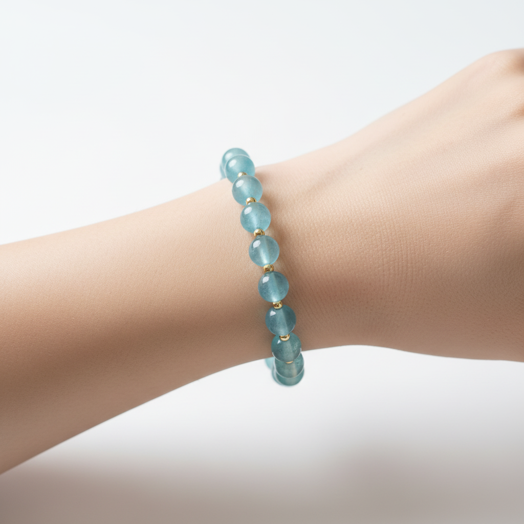 The Rowan Bracelet on Wrist. A close up of an arm, with a translucent blue color bead bracelet with gold filled beads in between each bead.