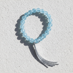 The Willa Bracelet - White Background Brighter Blue. There is a silver tassel that dangles from the bracelet. 