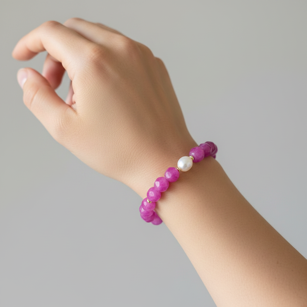 The Zinnia Bracelet on wrist. Shows a femaile arm and wrist, with a magenta unique shaped bead braelet. a pearl sitting in the front of the bracelet surrounded by gold spacers. 