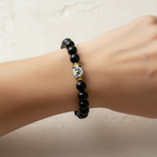 The Ziva Bracelet on wrist - gold spacers. This is a close up of a wrist. The bracelet on the wrist is black with a small rectangle spotted bead. Gold spacers surroundthe accent.